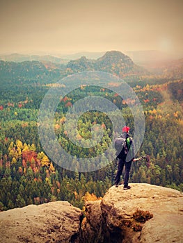 Tall hiker man with red cap, poles in hand and with big backpack stand on rock. Misty spring