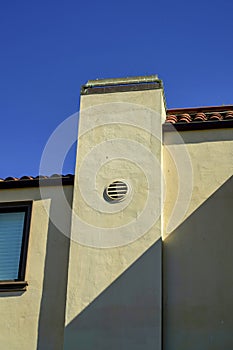 Tall house chimney with metal vents and stucco beige exterior wall with cement and visible windows and blue sky