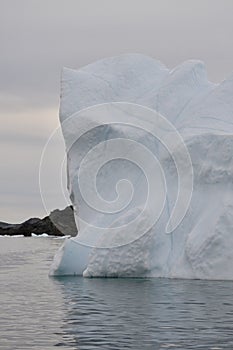 Tall iceberg stranded in Twillingate Harbour along rugged shoreline