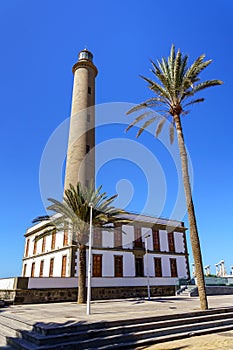 tall lighthouse over blue sky in summer next to large green palm tree on Maspalomas beach in the Canary Islands. spain. Europe