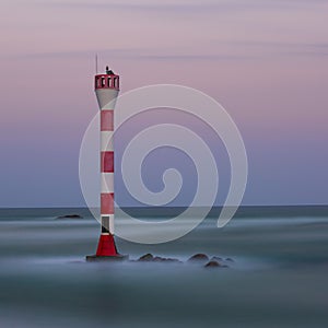 Tall lighthouse overlooking a quiet sea under a beautiful pink and purple sky at sunset