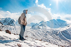 A tall man with a beard stands alone amid snow mountains. Way of life survival