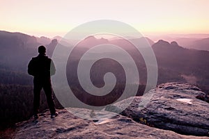 Tall man in black on cliff and watch to mountain sunrise.Silhouette in selfconfident pose