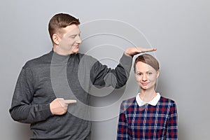 Tall man is showing height of short woman and pointing at her