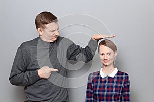 Tall man is showing height of short woman and pointing at her