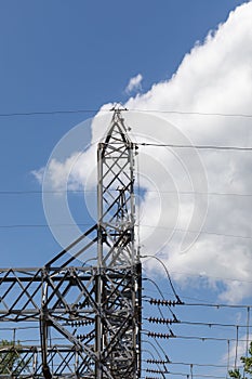 Tall metal trusses carrying electrical power lines and strain insulators silhouetted against a blue sky with dramatic white clouds