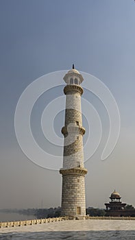 The tall minaret of the ancient Taj Mahal against a clear blue sky.