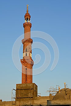 A tall minaret with golden ornament of a mosque that is under construction, minaret or tower aspiring to heaven, Islamic religion