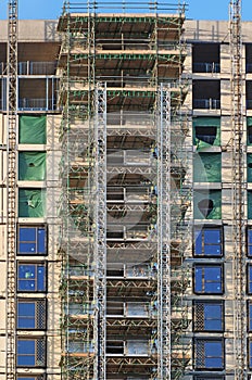 tall modern multistory apartment building under construction with scaffolding and hoist frames under a blue sky