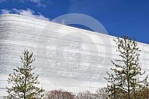 tall modern white building with green trees in front