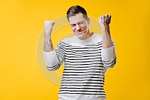 Tall muscular young man in a striped shirt making sucsess gesture over yellow