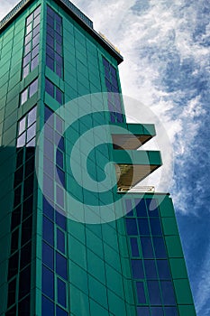 A tall office building in green against a blue sky and white clouds.