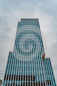 Tall office skyscraper with glass facade against stormy blue sky