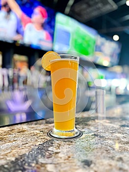 Tall pilsner glass full of draught beer on marble bar table with blurry beer tap and sport TV background at American restaurant in