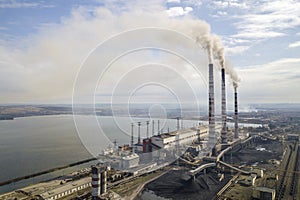 Tall pipes of power plant, white smoke on rural landscape, lake water and blue sky copy space background