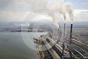 Tall pipes of power plant, white smoke on rural landscape, lake water and blue sky copy space background