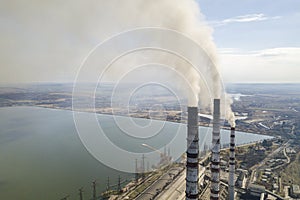 Tall pipes of power plant, white smoke on rural landscape, lake water and blue sky copy space background