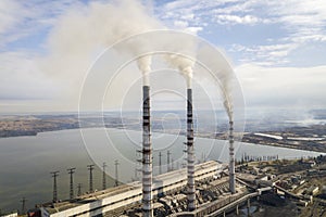 Tall pipes of power plant, white smoke on rural landscape, lake water and blue sky copy space background