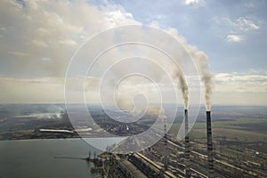 Tall pipes of power plant, white smoke on rural landscape, lake water and blue sky copy space background