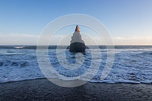 Tall pointy rock on beach shoreline with waves rolling in over sand