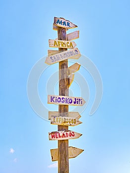 Tall post with colored wooden signboards pointing to various destinations and a beach services in Spanish