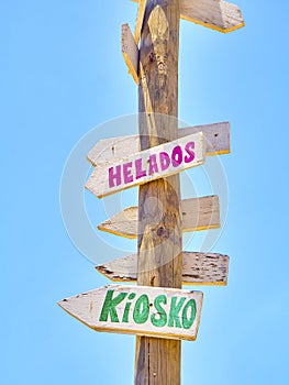 Tall post with colored wooden signboards pointing to various destinations and a beach services in Spanish
