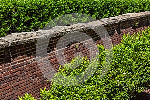 Tall red brick retaining wall with rough stone cap, shrubbery above and below