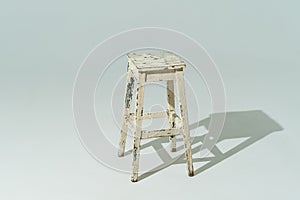 Tall retro stool or tabouret with peeling white paint on white background. Empty place