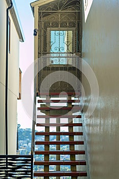 Tall see through staircase on hilltop house with flat brick steps and cement walls with metal protective door cover