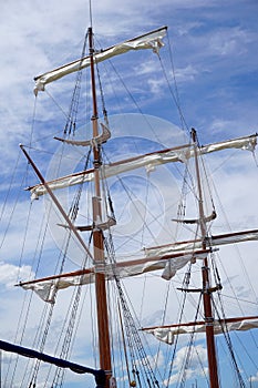 Tall ship mast with rolled sails, sky in background