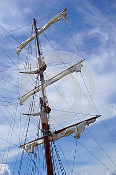 Tall ship mast with rolled sails, sky in background