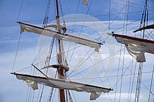 Tall ship mast with rolled sails, sky in background