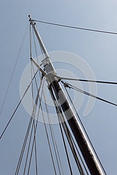 Tall ship mast with rope rigging lines, block and tackle, against a blue sky