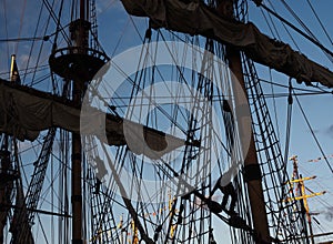 Tall ship masts and rigging silhouetted against a dramatic sky at sunset