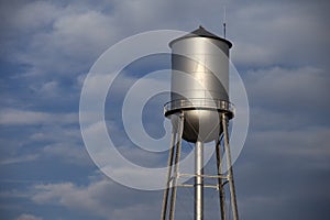 Tall silver water tower in front of a cloudy blue