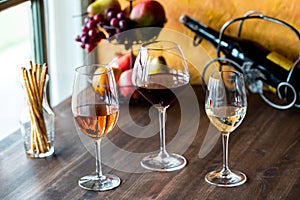 Tall stem glasses of rose, red and white wine on a wooden table