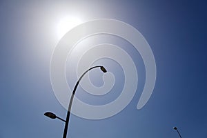 Tall street lamp on a blue sky background with a shining sun