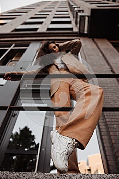 Tall stylish girl with oversized jacket posing near the railing and steps on the city background