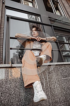 Tall stylish girl with oversized jacket posing near the railing and steps on the city background