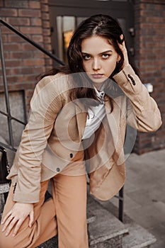 Tall stylish girl with oversized jacket posing near the railing and steps on the city background