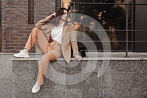 Tall stylish girl with oversized jacket posing near the railing and steps on the city background