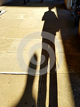 Tall sun lit Shadows haunt the paving stones London, strange long legs and head