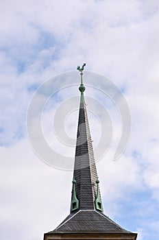 Tall tiled spire on a roof surmounted by a cock