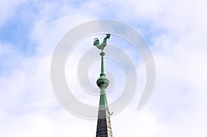 Tall tiled spire on a roof surmounted by a cock