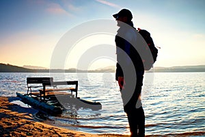 Tall tourist with backpack walk on beach at pedal boat in the sunset. Autumn at sea