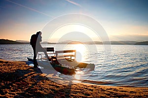 Tall tourist with backpack walk on beach at pedal boat in the sunset. Autumn at sea