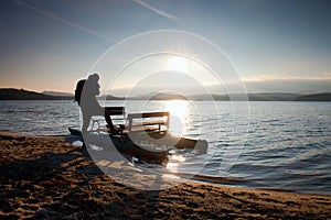 Tall tourist with backpack walk on beach at pedal boat in the sunset. Autumn at sea