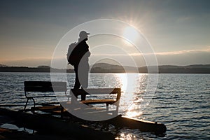 Tall tourist with backpack walk on beach at pedal boat in the sunset. Autumn at sea