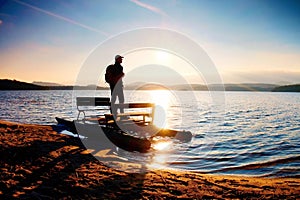 Tall tourist with backpack walk on beach at pedal boat in the sunset. Autumn at sea