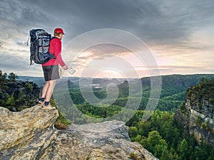 Tall tourist with big backpack looking in paper map. Wild hilly nature park. Hiker looking for new locations and landmarks to